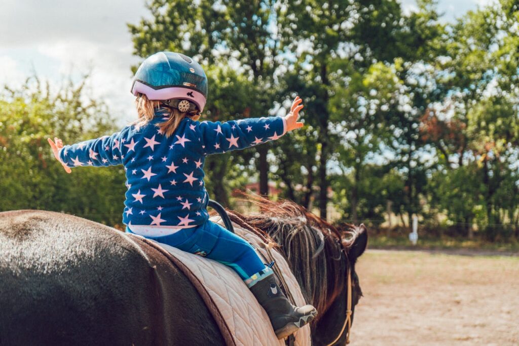 A child confidently rides a horse outdoors, wearing a helmet and star-patterned jacket.